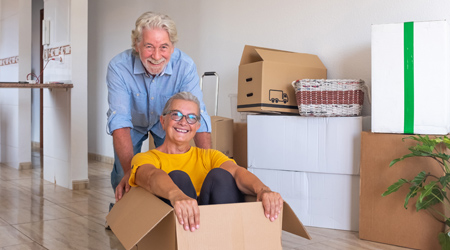 happy person sitting in a moving box being pushed across floor by happy man